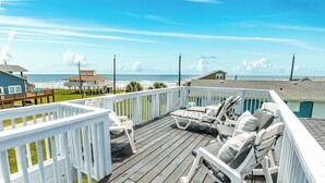 A wooden deck with white railings, white rocking chairs, and a view of the ocean. - Willy's Place: 3rd Row Gulf View Home with Updated Interior & Rooftop Sun Deck (Galveston)