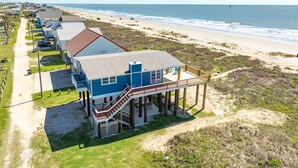 Ein Strandgrundstück mit einem blauen Haus, das auf Stelzen steht, einem Sandstrand und freiem Blick auf den Ozean.