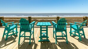 Eine Holzterrasse mit Tisch und vier Stühlen, mit Blick auf einen Strand und den dahinterliegenden Ozean.