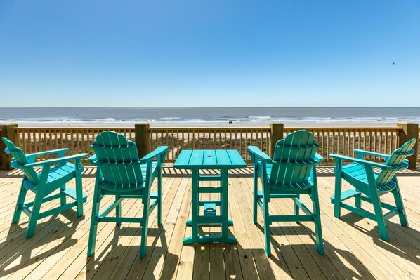 A wooden deck with a table and four chairs, overlooking a beach with the ocean in the background. - Panoramic Gulf Views @ Beachfront Home w/ Updated Interior, Free Wifi (Galveston)