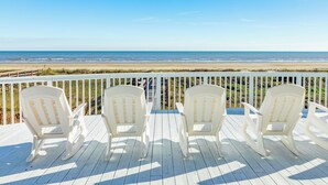 Una terraza con tres sillas Adirondack blancas mirando a la playa.