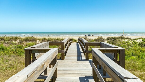 Un paseo marítimo de madera que conduce a una playa con cielo despejado.