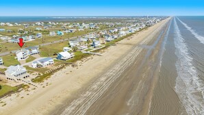 Luchtbeeld van een kustgebied met woonhuizen aan het strand, een heldere lucht en een zichtbare weg.