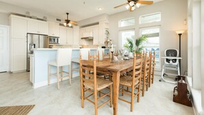 Een ruime keuken met witte kastjes, een centraal eiland, houten stoelen en een plafondventilator.