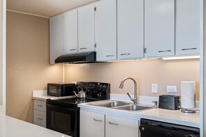 Une cuisine moderne avec des meubles blancs, une cuisinière noire, un four à micro-ondes et un lave-vaisselle.