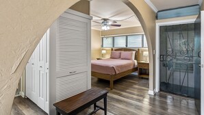 A bedroom with a bed, a bench, a ceiling fan, and a sliding glass door. - Kalani Kai#104 1st Floor, Remodeled Unit in Heart of Kona Town! Best location (Kailua Kona)