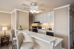 Une cuisine avec un plan de travail blanc, un ventilateur de plafond et un tabouret de bar.