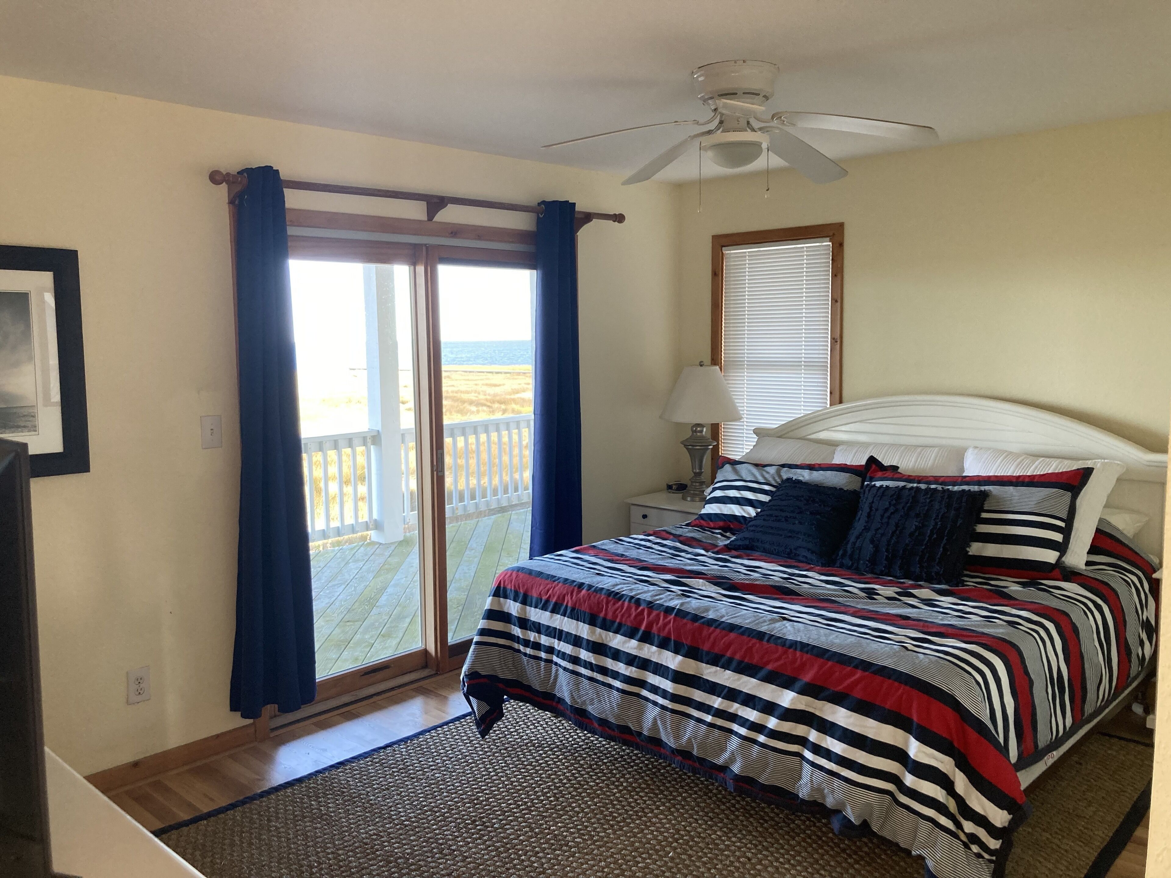 Une chambre à coucher comprenant un lit, une table de chevet, une lampe, un ventilateur de plafond et une vue sur l’extérieur grâce à une porte coulissante.