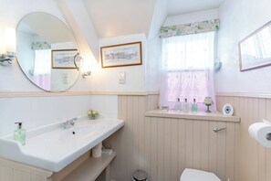 Et badeværelse med et stort spejl, en vask, et toilet og et vindue med gardiner.