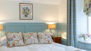A neatly made bed with floral-patterned pillows, a bedside table with a lamp, and a framed floral artwork on the wall. - The Firs (Pitlochry)