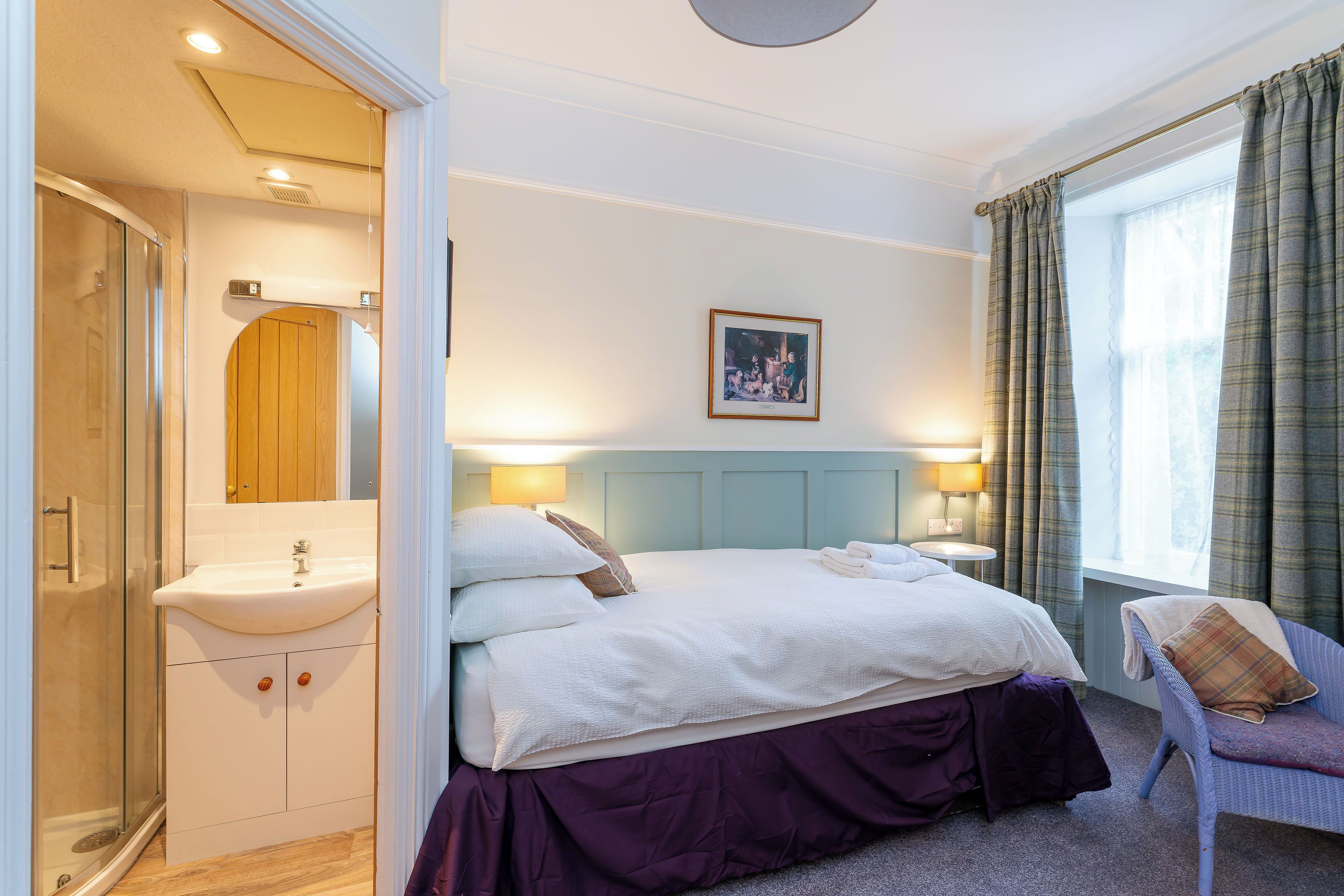A hotel room with a bed, a chair, a sink, and a shower.