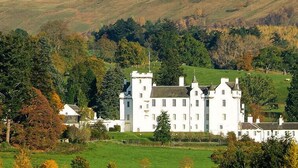 A large white castle-like building surrounded by lush greenery and hills. - The Firs (Pitlochry)