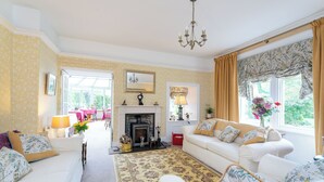 A living room with a fireplace, a sofa set, a patterned rug, and a window with curtains. - The Firs (Pitlochry)