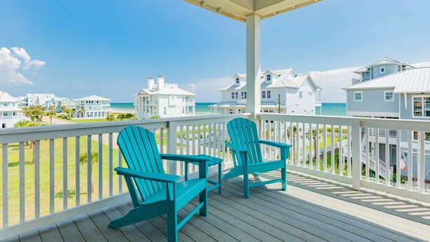 A wooden deck with two turquoise Adirondack chairs, overlooking a beach with white houses and a clear blue sky. - 2nd Row Dog Friendly Home w/ Gulf views, 2 Decks, Screened Area (Galveston)