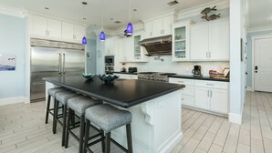 A modern kitchen with white cabinetry, a large island with bar stools, stainless steel appliances, and blue pendant lights. - 2nd Row Dog Friendly Home w/ Gulf views, 2 Decks, Screened Area (Galveston)