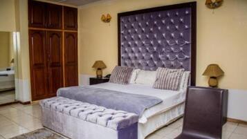 A bedroom with a large bed, a wooden wardrobe, two bedside lamps, and a bench.