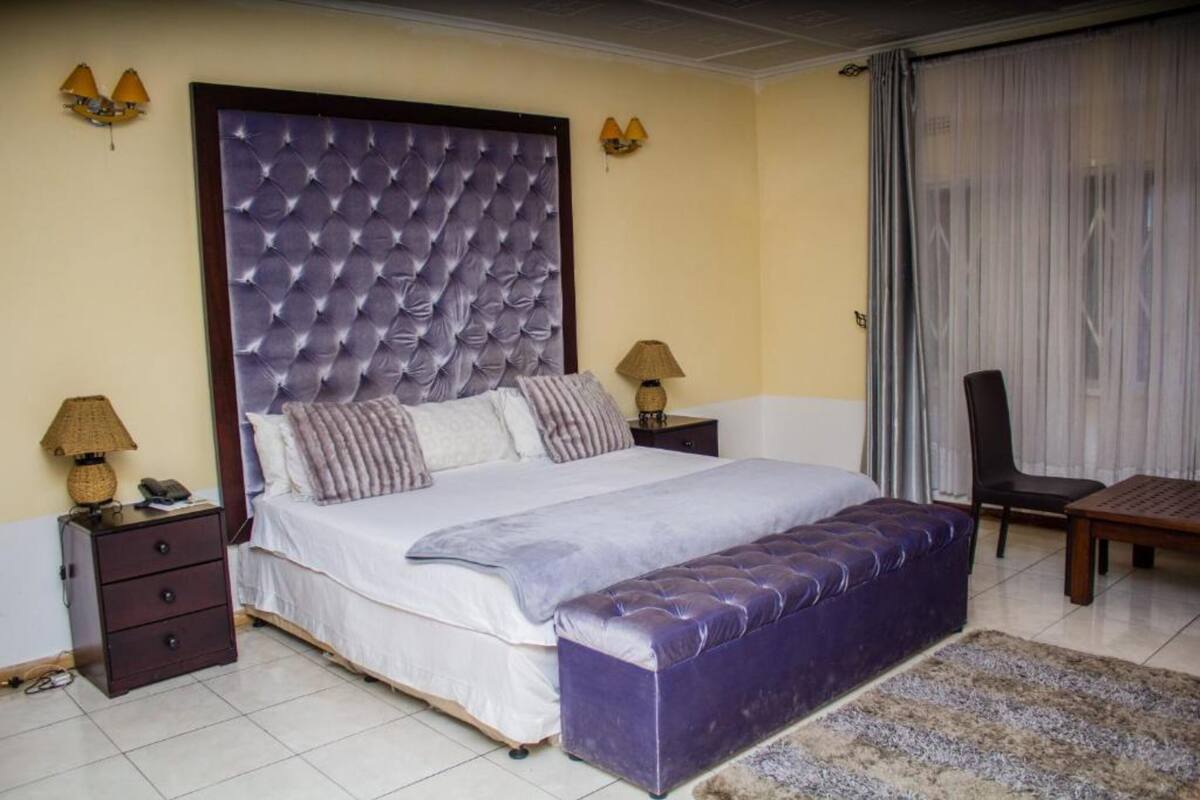 A bedroom with a tufted headboard, a large bed with multiple pillows, a bench, two bedside tables with lamps, and a chair.