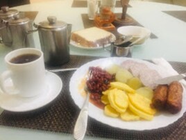 Una mesa de desayuno con un plato de frutas cortadas, una taza de café y un tazón pequeño de mermelada.