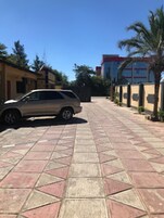 Un camino pavimentado con un coche aparcado, un edificio de techo rojo y una palmera.