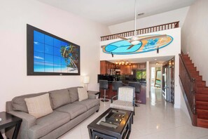 Un salon avec un canapé, une table basse et un tableau représentant une scène de plage.
