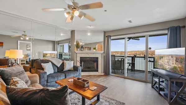 A spacious living room with a fireplace, comfortable seating, a balcony with a scenic view, and a television.