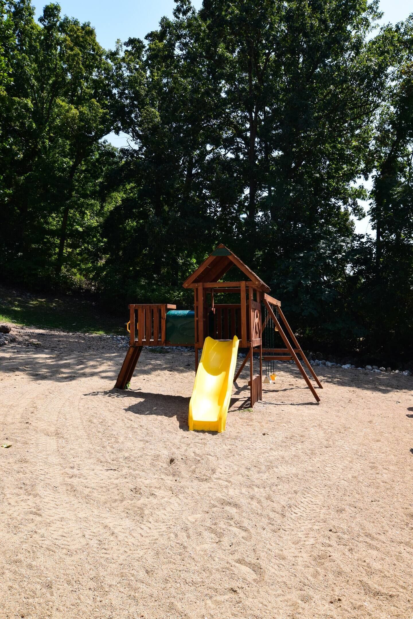 Eine Holzspielkonstruktion mit Rutsche, umgeben von Sand und Bäumen.
