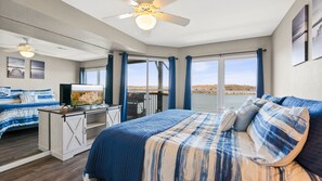 A bedroom with a large bed, a desk with a TV, and a view of a body of water.