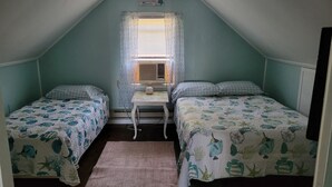 Una habitación pequeña y triangular con dos camas, una mesa y una ventana con cortinas.
