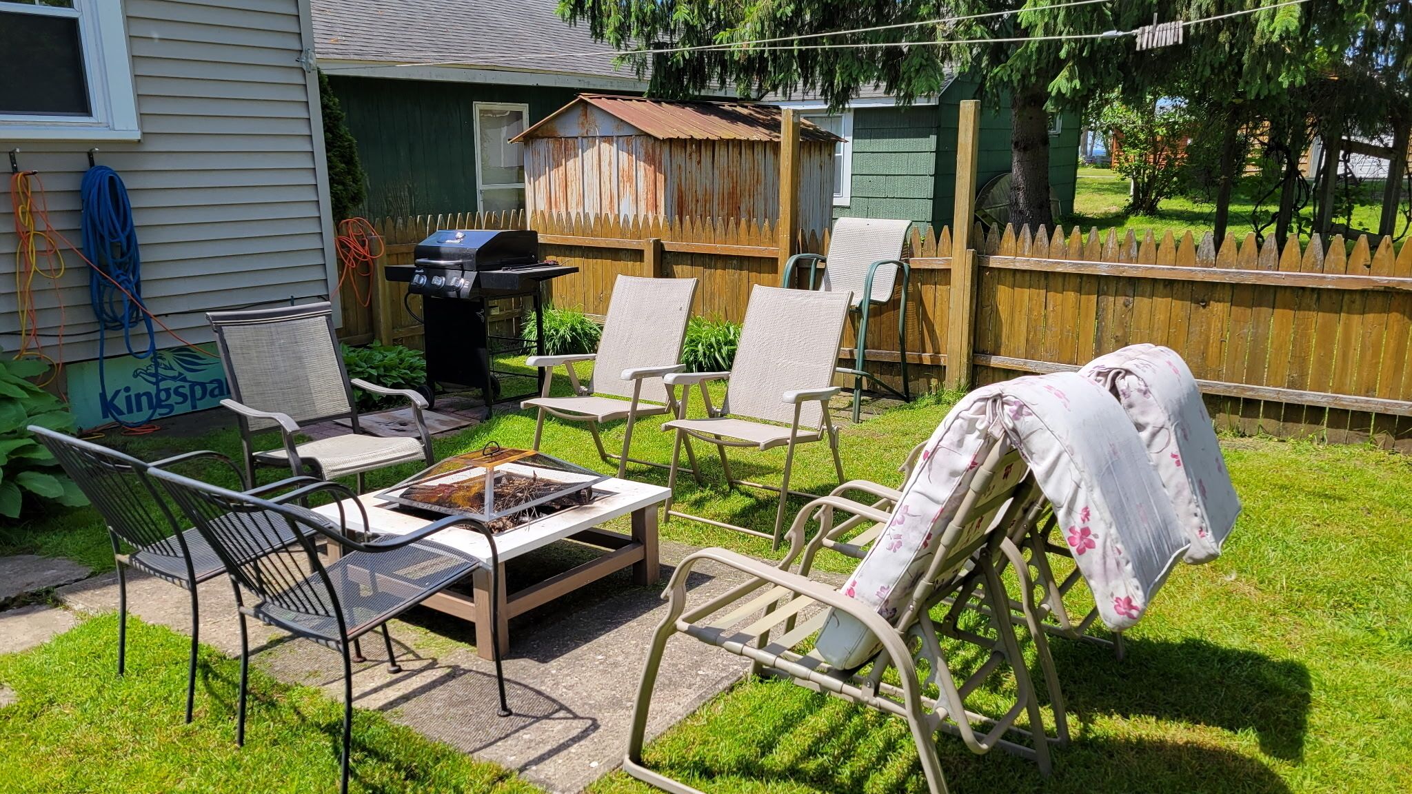 Een achtertuin met een barbecue, tuinmeubilair en een overdekte picknicktafel.