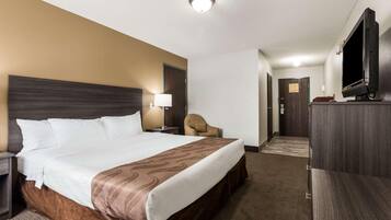 A hotel room with a large bed, a TV, a chair, and a desk.