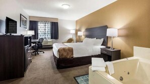 A hotel room with a bed, a desk, a chair, a TV, a lamp, and a bathtub. - Quality Inn Clare (Clare)