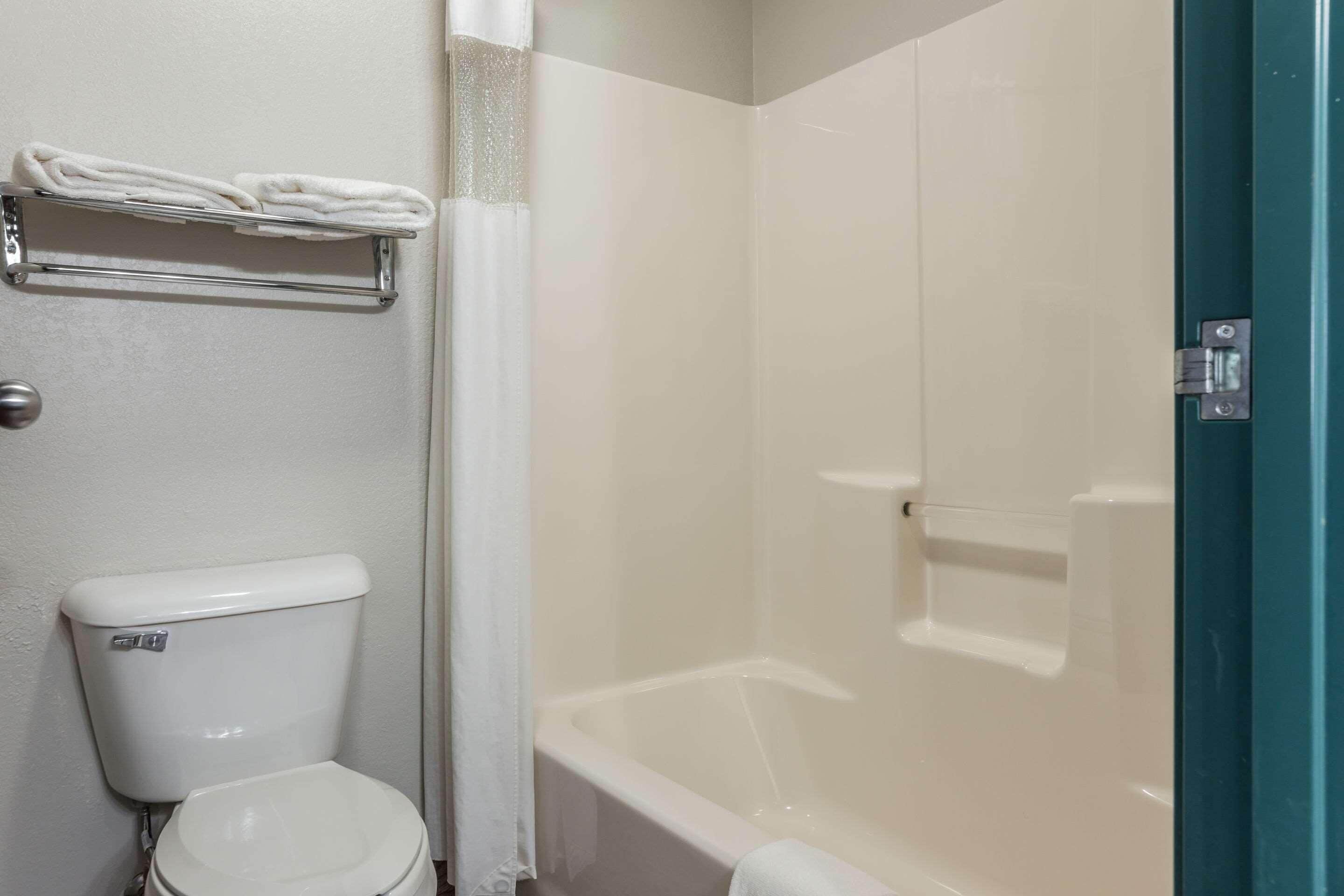 Un baño con inodoro, toallero con toallas dobladas, cortina de ducha y bañera.