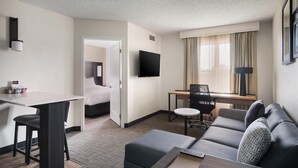 Ein Hotelzimmer mit Bett, Schreibtisch, Sofa, Fernseher und einem Fenster mit Vorhängen.