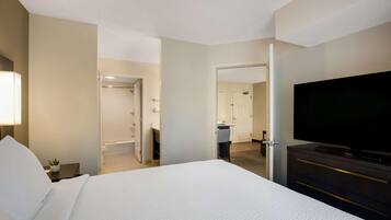 A hotel room with a large bed, a TV, a desk with a lamp, and a bathroom visible through an open door.