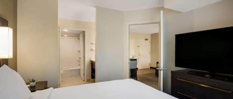 A hotel room with a large bed, a TV, a desk with a lamp, and a bathroom visible through an open door.