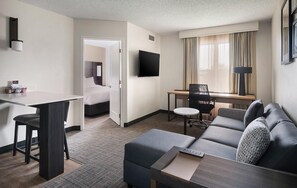 Habitación de hotel con cama, escritorio, sofá, televisión y ventana con cortinas.