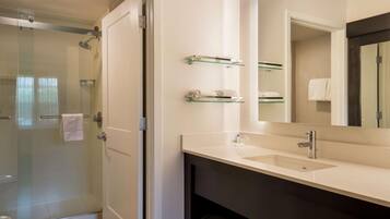 A modern bathroom with a glass shower enclosure, a large mirror, and a vanity with a sink and towel racks.