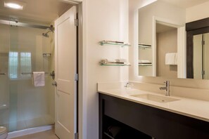 Ein modernes Badezimmer mit Duschkabine aus Glas, großem Spiegel und Waschtisch mit Spüle und Handtuchhaltern.
