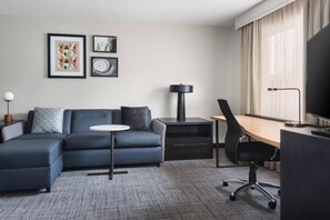 Een moderne hotelkamer met een modulaire bank, een bureau, een stoel, een klein rond tafeltje en een televisie.
