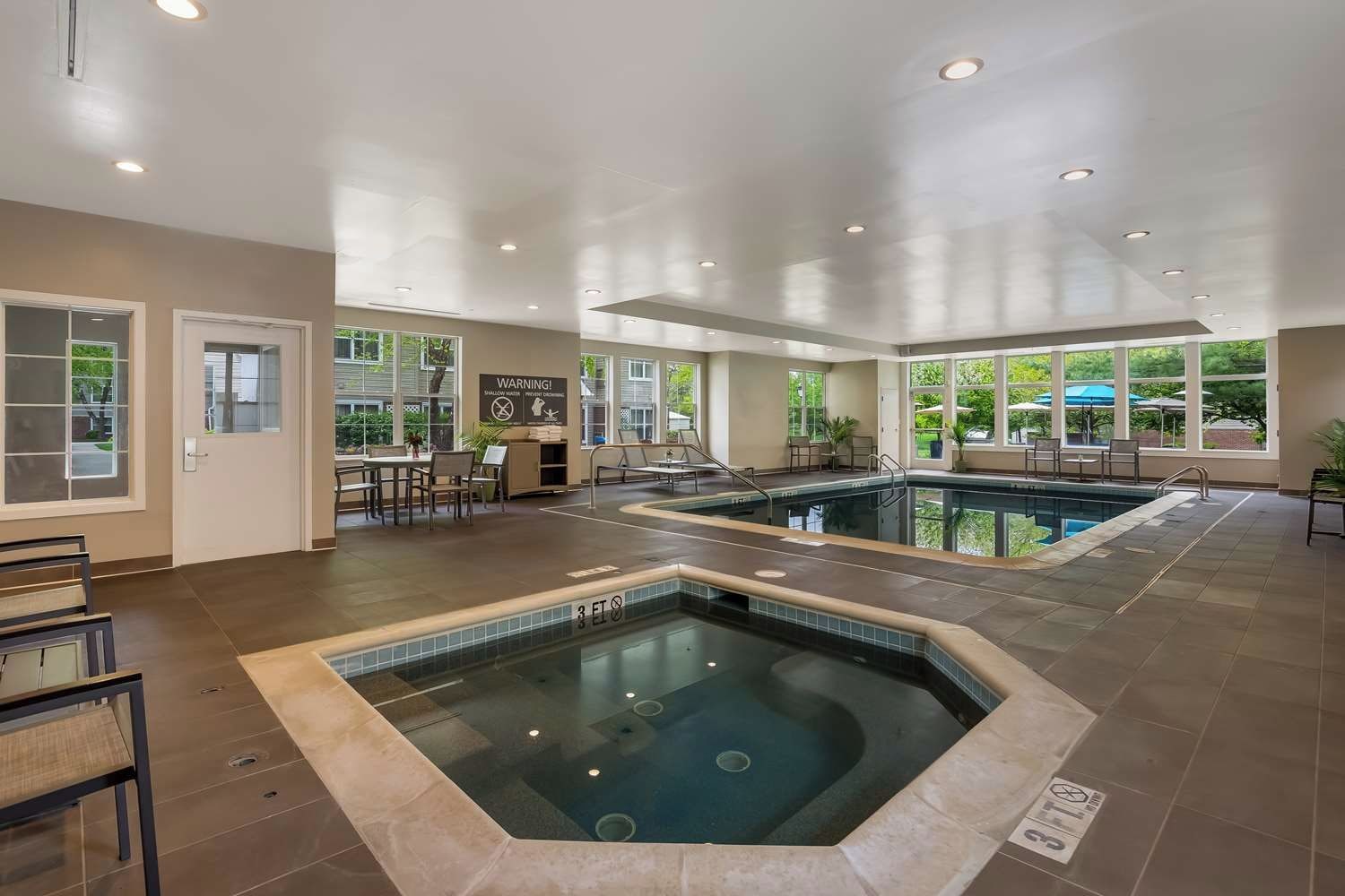 A hotel indoor pool area with a hot tub, seating, and a view of the outdoors.