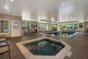 Un espace piscine intérieure d’hôtel avec un jacuzzi, des sièges et une vue sur l’extérieur.