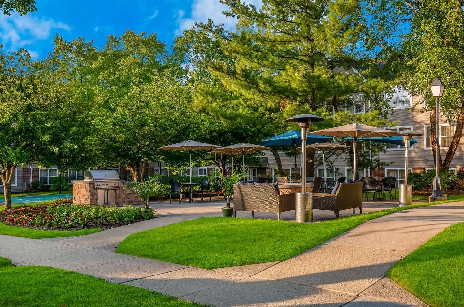 An outdoor patio area with seating, a barbecue grill, and umbrellas providing shade.