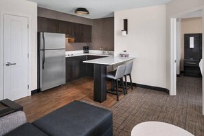 Een kleine keuken met een koelkast, een koffiezetapparaat en een eethoek met een tafel en stoelen.