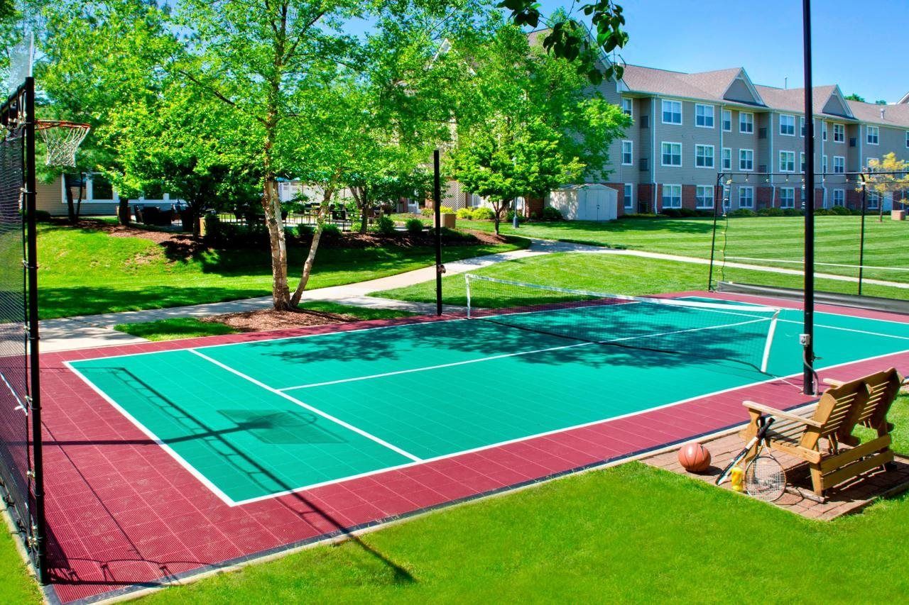An outdoor basketball court with a net, a bench, and a basketball.