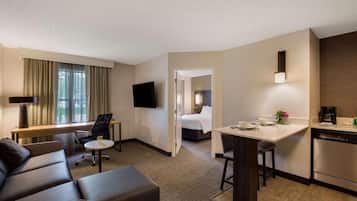 A hotel room with a sofa, a desk, a bed, a TV, and a kitchen area.