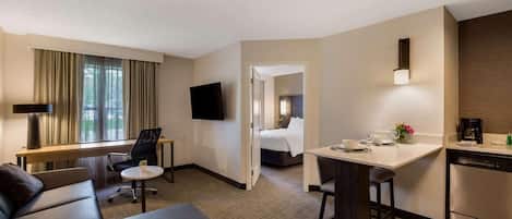 A hotel room with a sofa, a desk, a bed, a TV, and a kitchen area.