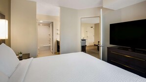 Ein Hotelzimmer mit einem großen Bett, einem Fernseher, einem Schreibtisch mit Lampe und einem durch eine geöffnete Tür einsehbarer Badezimmer.