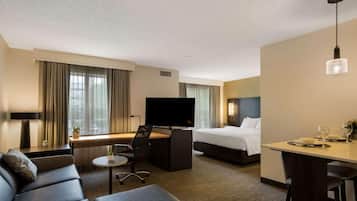 A hotel room with a bed, a desk with a TV, a sofa, a dining table, and a small round table with a chair.