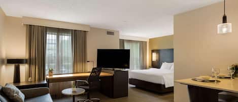 A hotel room with a bed, a desk with a TV, a sofa, a dining table, and a small round table with a chair.