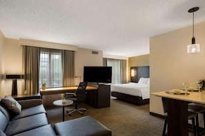Une chambre d’hôtel comprenant un lit, un bureau avec une télévision, un canapé, une table à manger et une petite table ronde avec une chaise.
